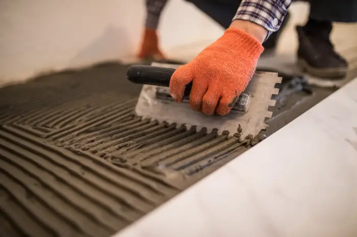 Artisan réalisant un ragréage fibré sur un ancien plancher avant la pose de carrelage